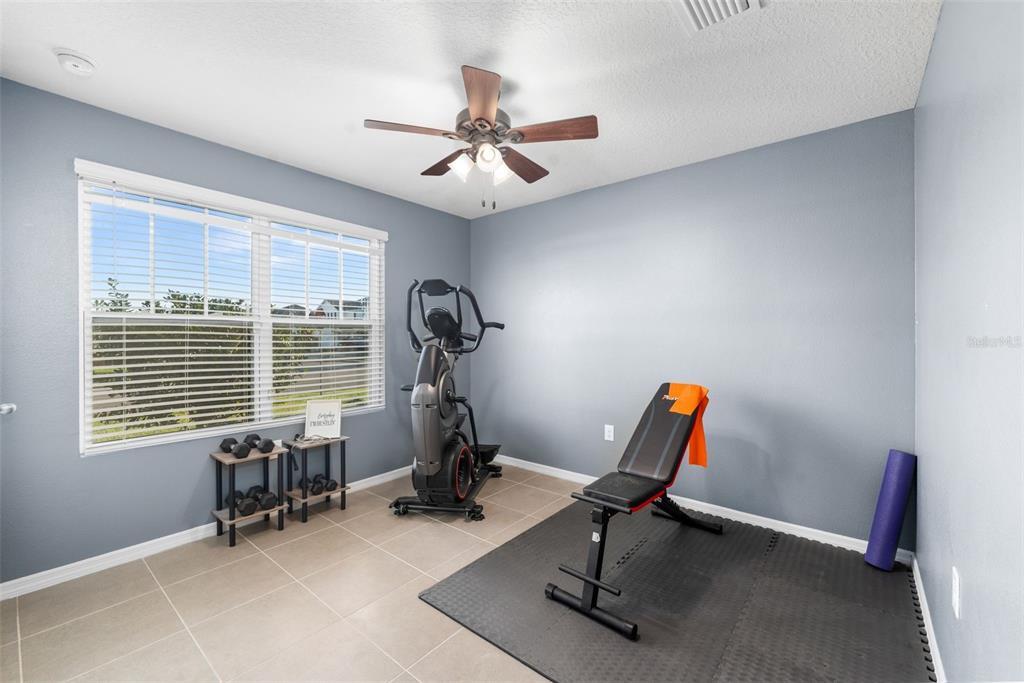 A home gym with light blue walls, tile flooring, an elliptical machine, and a weight bench — 25119 NW 8TH ROAD, NEWBERRY, FL