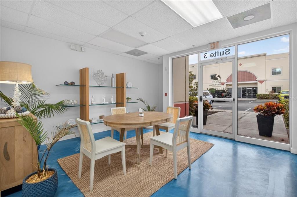 A bright office space features a round wooden table, white chairs, and blue floors — 6321 PORTER UNIT 3, SARASOTA, FL