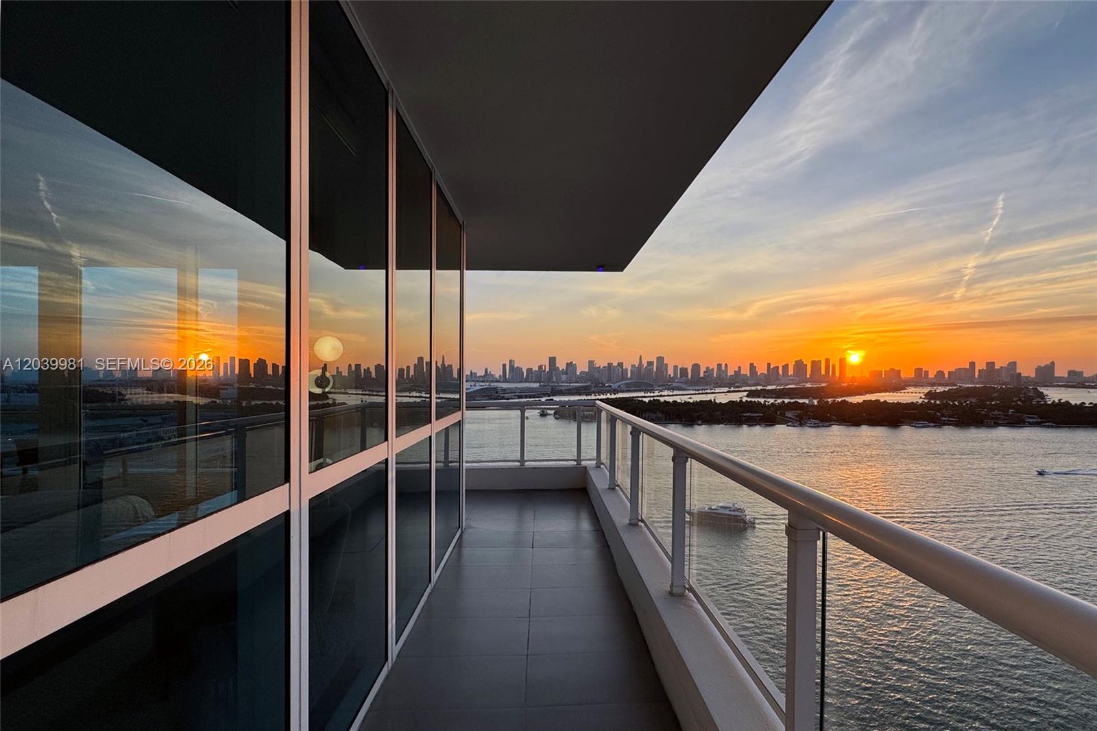 A balcony with glass railings overlooks a bay and city skyline at sunset — 540 West Ave # 2114, Miami Beach FL 33139, MIAMI BEACH, FL