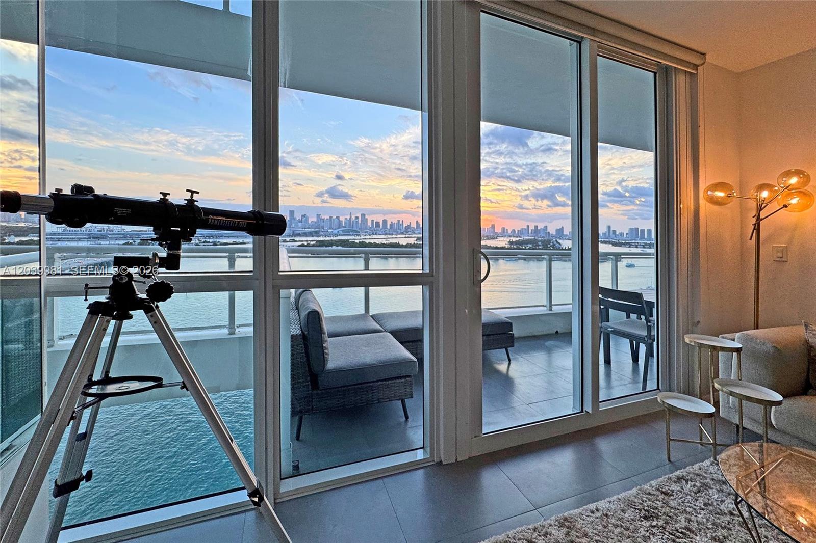 A living room features floor-to-ceiling windows overlooking a balcony, water, and a city skyline — 540 West Ave # 2114, Miami Beach FL 33139, MIAMI BEACH, FL