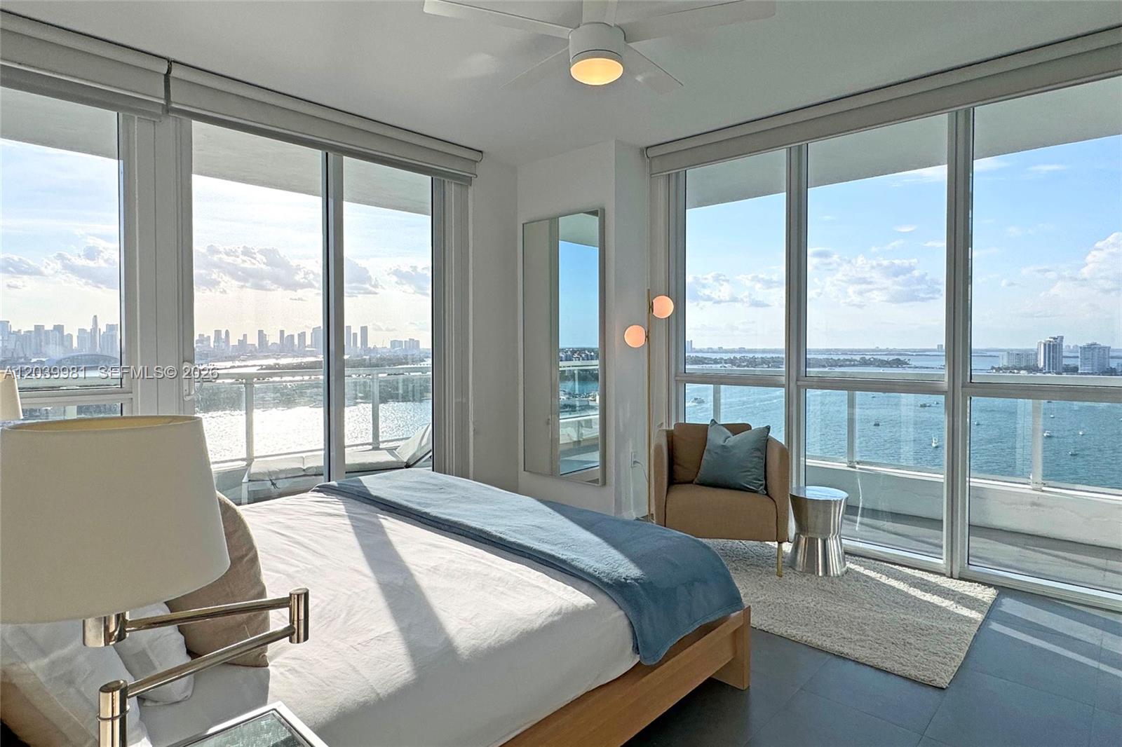 A bedroom features a bed, a chair, and floor-to-ceiling windows overlooking a city skyline — 540 West Ave # 2114, Miami Beach FL 33139, MIAMI BEACH, FL