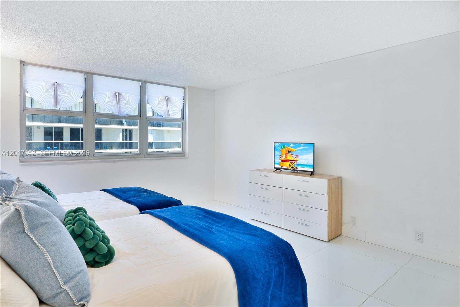 A bedroom features two beds with blue throws, a white dresser, and large windows — 9511 Collins Ave # 901, Surfside FL 33154, SURFSIDE, FL