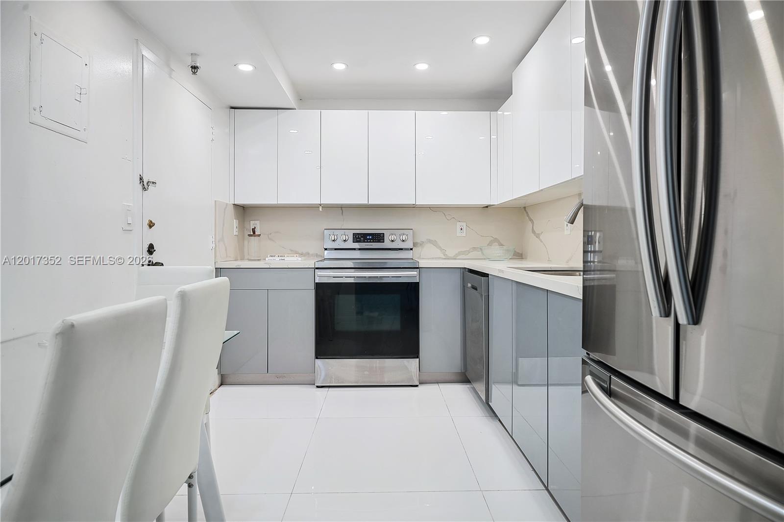 A modern kitchen features white upper cabinets, grey lower cabinets, and stainless steel appliances — 9511 Collins Ave # 901, Surfside FL 33154, SURFSIDE, FL
