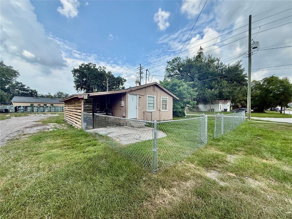 A small, tan, single-story house with a fenced yard and a covered side patio — 3908 S NASHVILLE AVENUE, ORLANDO, FL