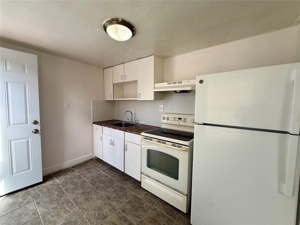 A small kitchen features white cabinets, a white stove, a white refrigerator, and tiled flooring — 3908 S NASHVILLE AVENUE, ORLANDO, FL