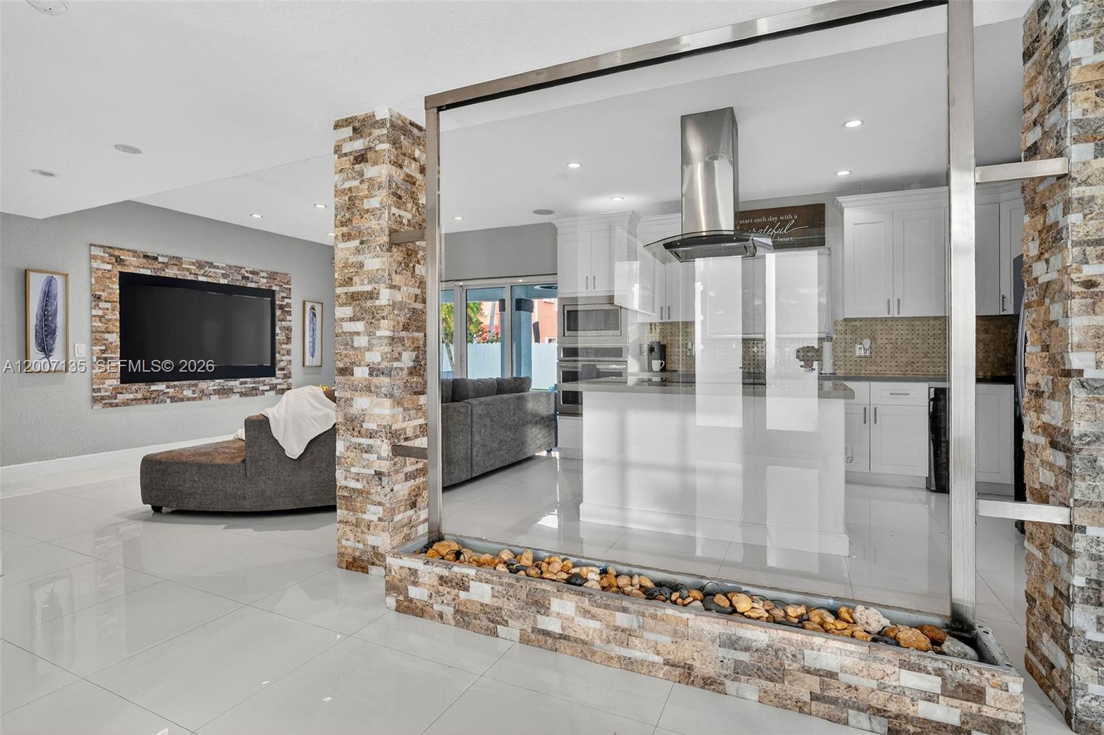A modern kitchen is separated from the living area by a glass-walled indoor rock feature — 5161 SW 159th Ct, Miami FL 33185, MIAMI, FL