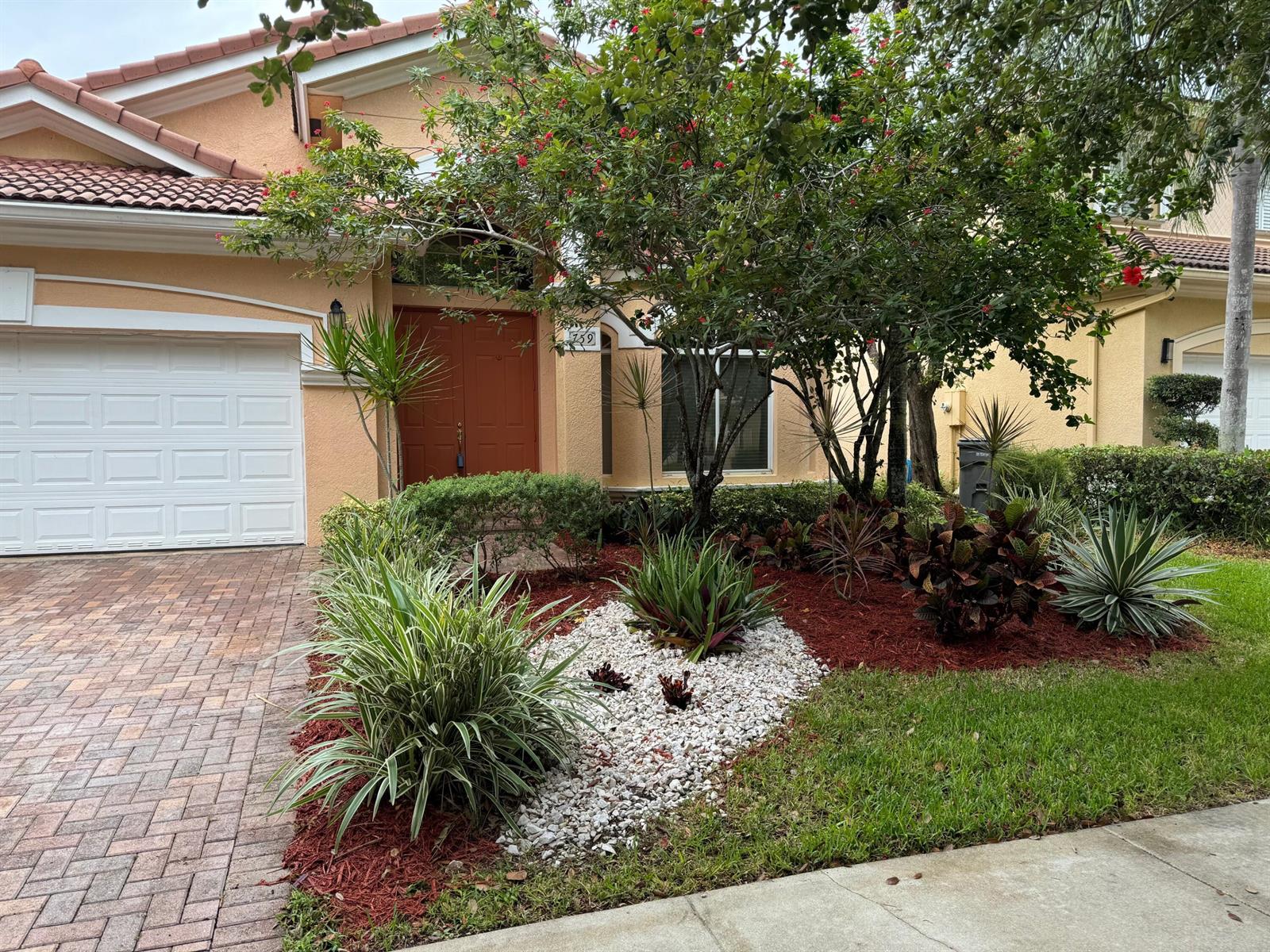 The exterior of a single-story house features a brick driveway, red mulch, and landscaping — 759 Gazetta Way, West Palm Beach FL 33413, WEST PALM BEACH, FL