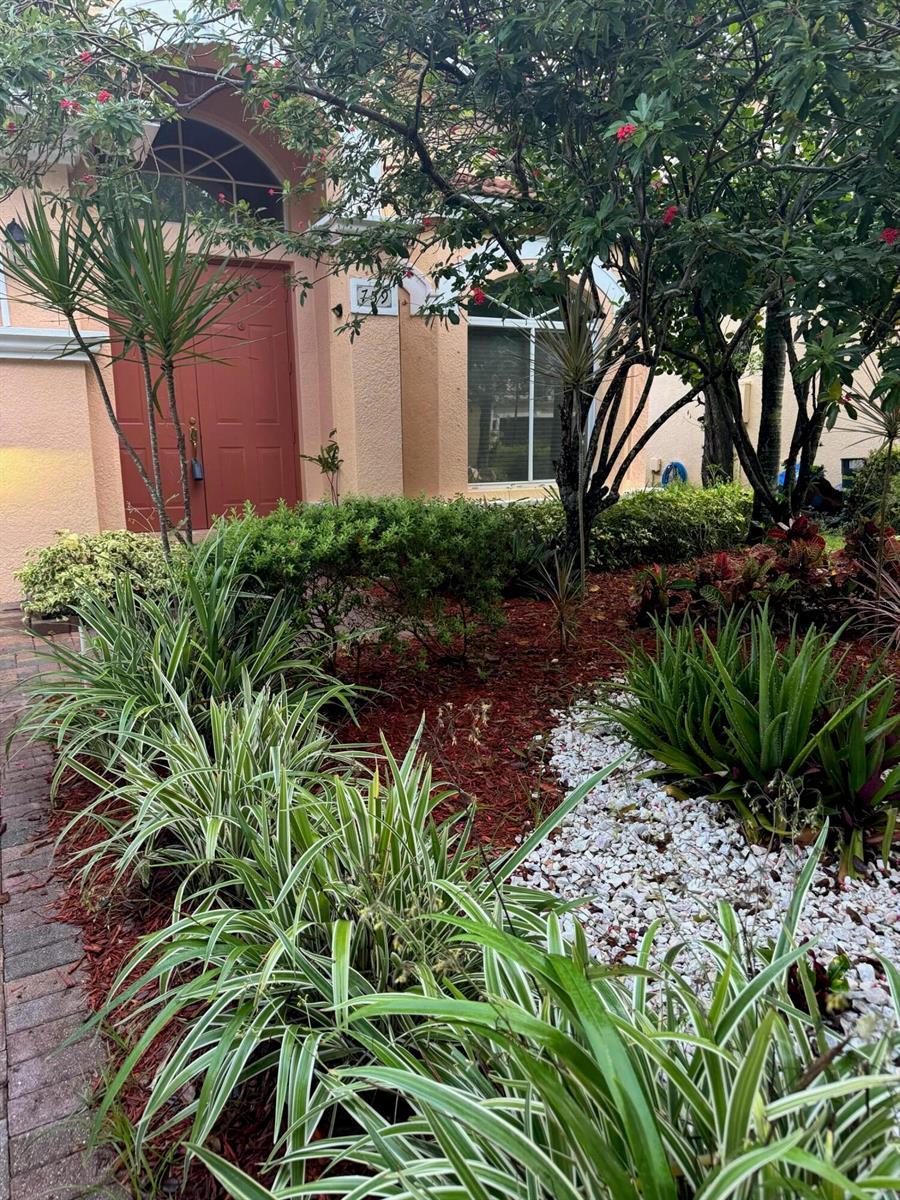 A front exterior view of a house featuring a red door and landscaped garden beds — 759 Gazetta Way, West Palm Beach FL 33413, WEST PALM BEACH, FL