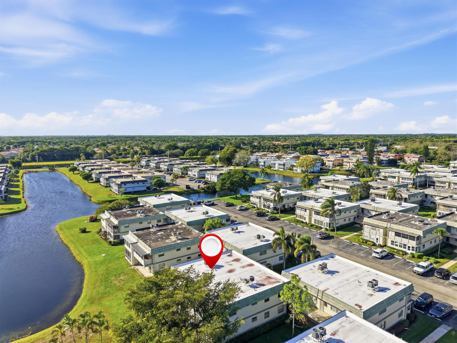 An aerial view shows a multi-story apartment complex with flat roofs situated near a lake — 710 Monaco O, Delray Beach FL 33446, DELRAY BEACH, FL