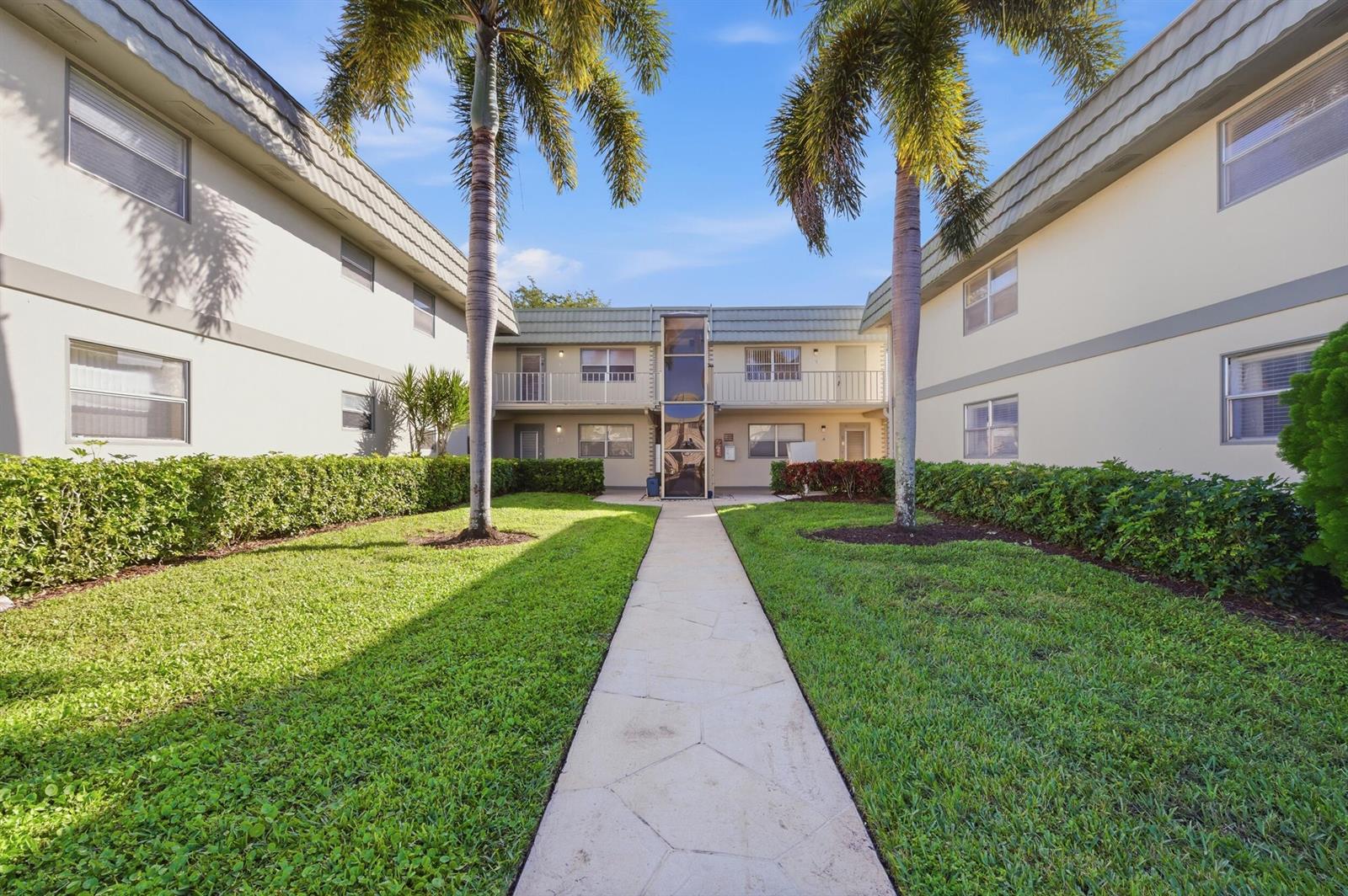A walkway leads between two apartment buildings with palm trees and manicured hedges — 710 Monaco O, Delray Beach FL 33446, DELRAY BEACH, FL