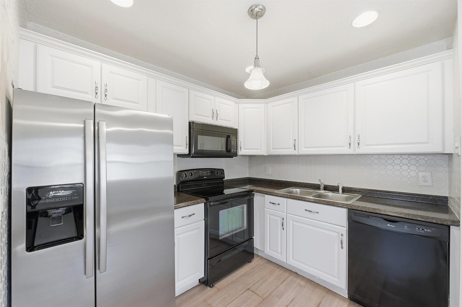 A kitchen features white cabinets, dark countertops, stainless steel appliances, and a light-colored tile floor — 710 Monaco O, Delray Beach FL 33446, DELRAY BEACH, FL