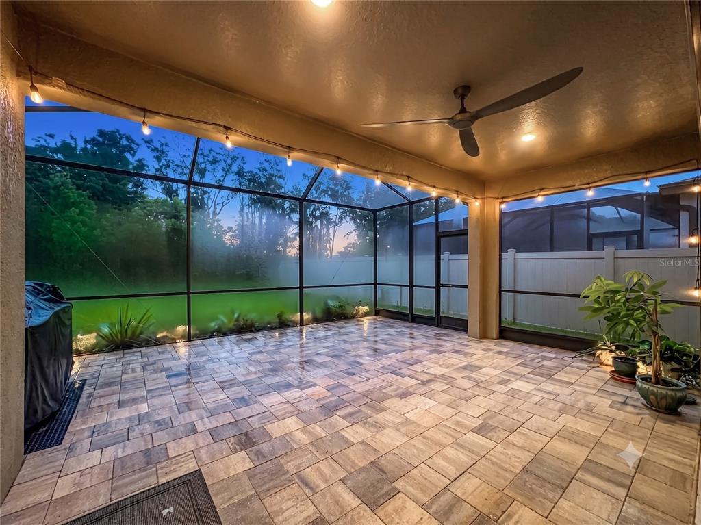 A screened-in patio features paver flooring, a ceiling fan, and string lights at dusk — 14654 HORSE TROT ROAD, LITHIA, FL