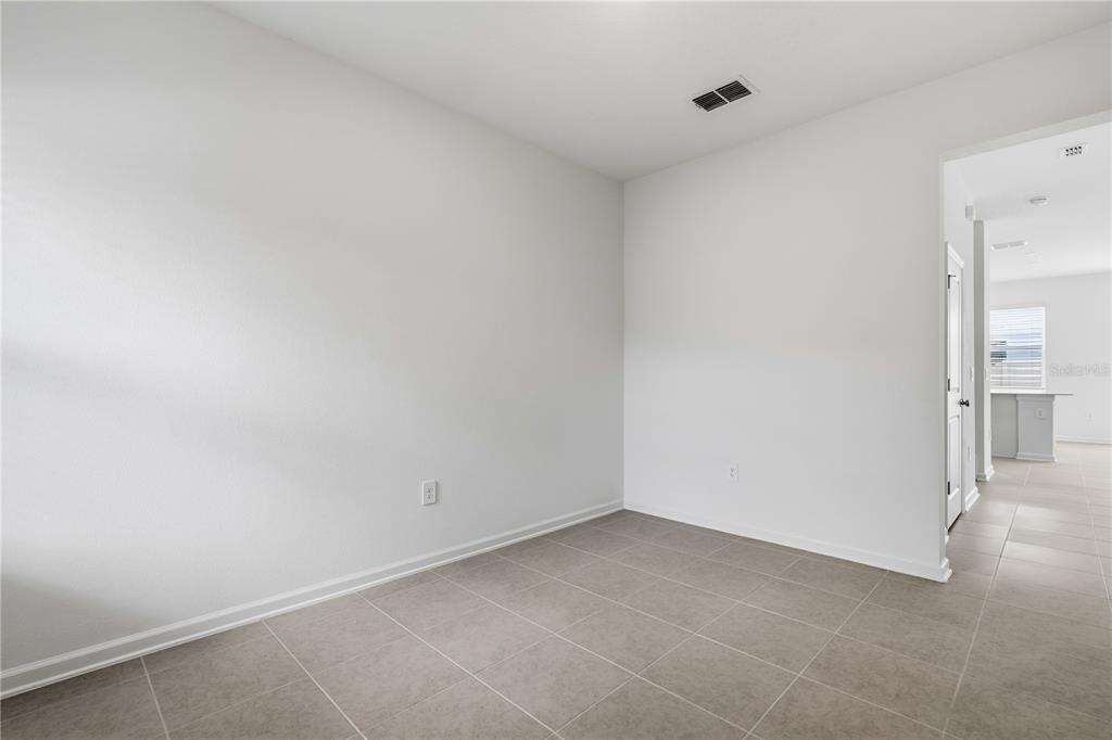 An empty room with white walls, tile flooring, and a doorway leading to a kitchen — 3092 CHROMATIC STREET, KISSIMMEE, FL