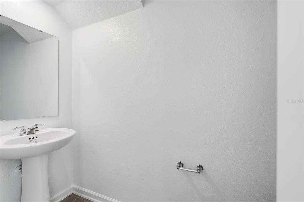 A minimalist half bathroom features a white pedestal sink, a wall mirror, and a toilet paper holder — 3092 CHROMATIC STREET, KISSIMMEE, FL