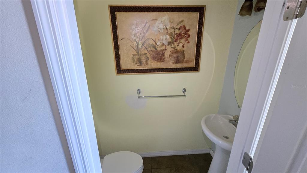 A small bathroom features a pedestal sink, a toilet, and a framed floral wall print — 1507 TALISKER DRIVE, CLEARWATER, FL