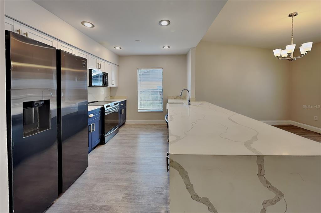 A kitchen features a large quartz island, dark blue lower cabinets, and stainless steel appliances — 2709 MANOR HILL DRIVE, BRANDON, FL