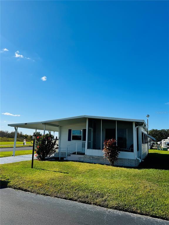 A single-story manufactured home features a screened-in porch and an attached carport — 320 ALOHA DRIVE, HAINES CITY, FL