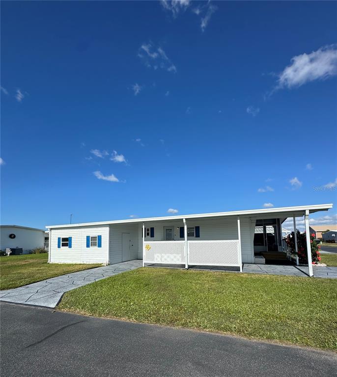A single-story manufactured home features white siding, blue shutters, and a covered front patio — 320 ALOHA DRIVE, HAINES CITY, FL