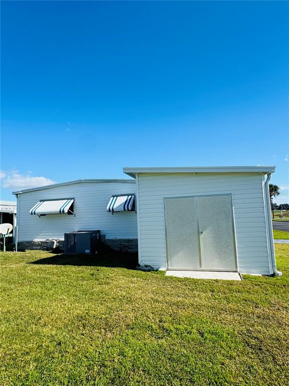 The exterior of a white mobile home features two window awnings and a storage shed — 320 ALOHA DRIVE, HAINES CITY, FL