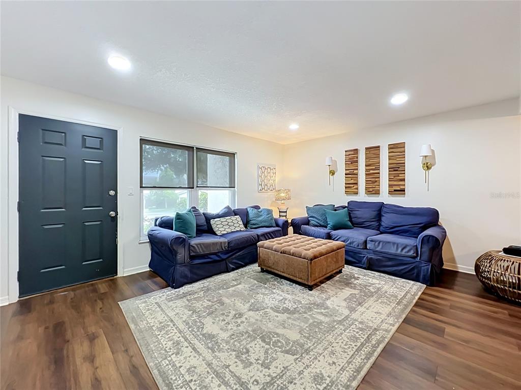 A living room features two blue sofas, a brown ottoman, and a patterned area rug — 603 WAVERLY LANE UNIT 405B, MAITLAND, FL