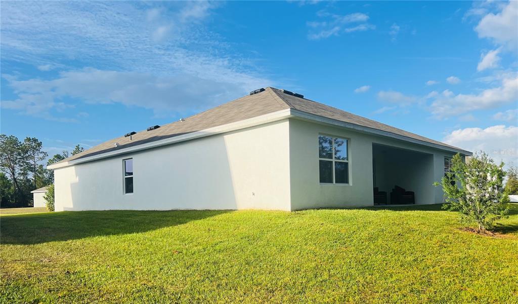 The exterior rear view of a white stucco house with a covered patio and lawn — 51 HICKORY COURSE TRAIL, OCALA, FL