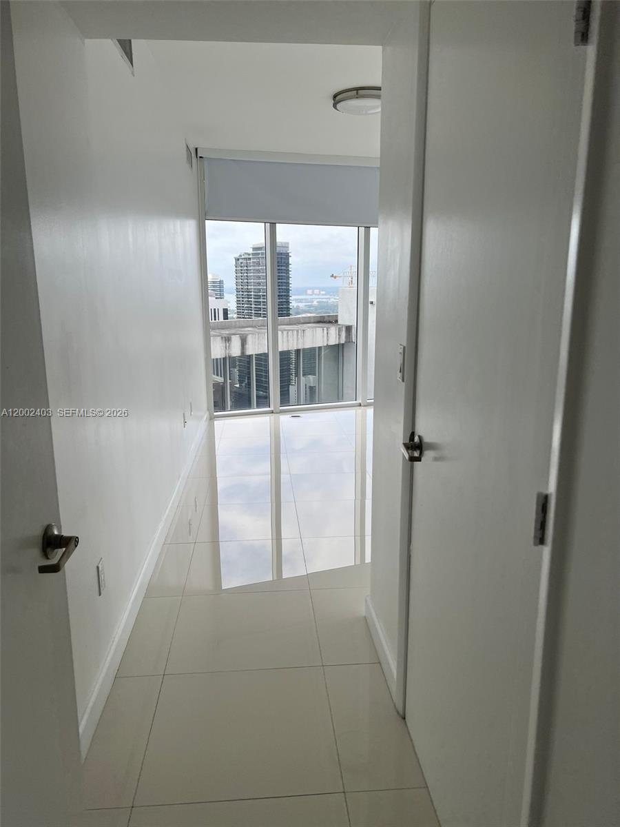 A narrow hallway with white walls and tile flooring leads to a floor-to-ceiling window — 475 Brickell Ave # 5508, Miami FL 33131, MIAMI, FL