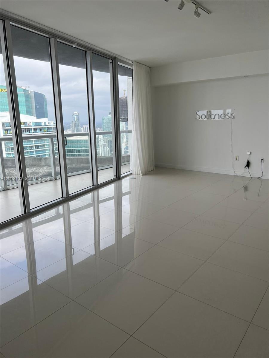 An empty room features white tile floors, floor-to-ceiling windows, and a city skyline view — 475 Brickell Ave # 5508, Miami FL 33131, MIAMI, FL