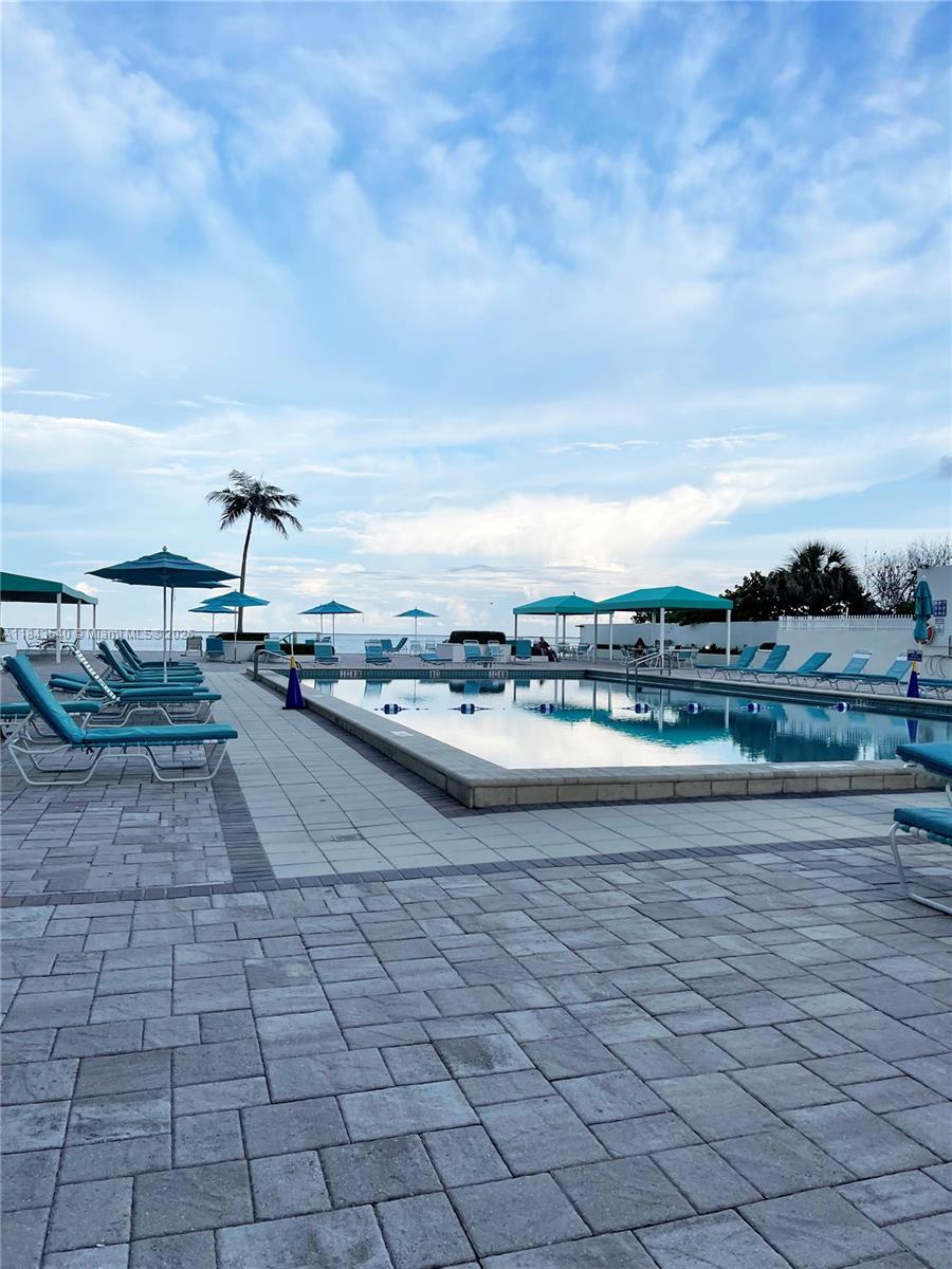 A swimming pool with lounge chairs and umbrellas on a paved deck overlooking the ocean — 3725 S Ocean Dr # 415, Hollywood FL 33019, HOLLYWOOD, FL