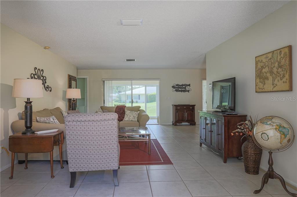 A living room features tile flooring, a beige sofa, a patterned armchair, and a globe — 6986 W COUNTRY CLUB DRIVE N UNIT 6986, SARASOTA, FL