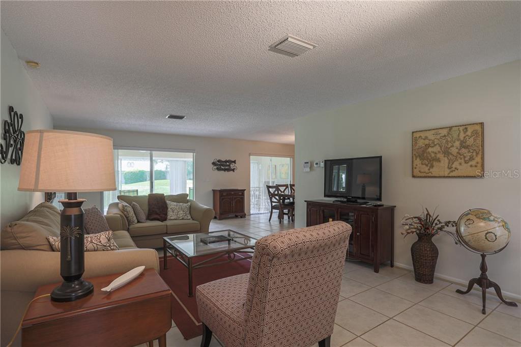 A living room with tile floors, a patterned armchair, a sofa, and a television console — 6986 W COUNTRY CLUB DRIVE N UNIT 6986, SARASOTA, FL