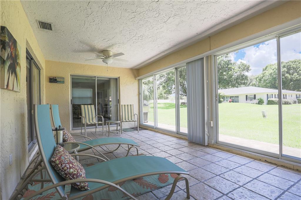 A sunroom with tile flooring, lounge chairs, and sliding glass doors overlooking a grassy yard — 6986 W COUNTRY CLUB DRIVE N UNIT 6986, SARASOTA, FL