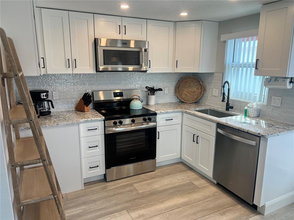 A kitchen features white cabinets, stainless steel appliances, granite countertops, and light wood-look flooring — 6154 MIDNIGHT PASS ROAD UNIT D02, SARASOTA, FL
