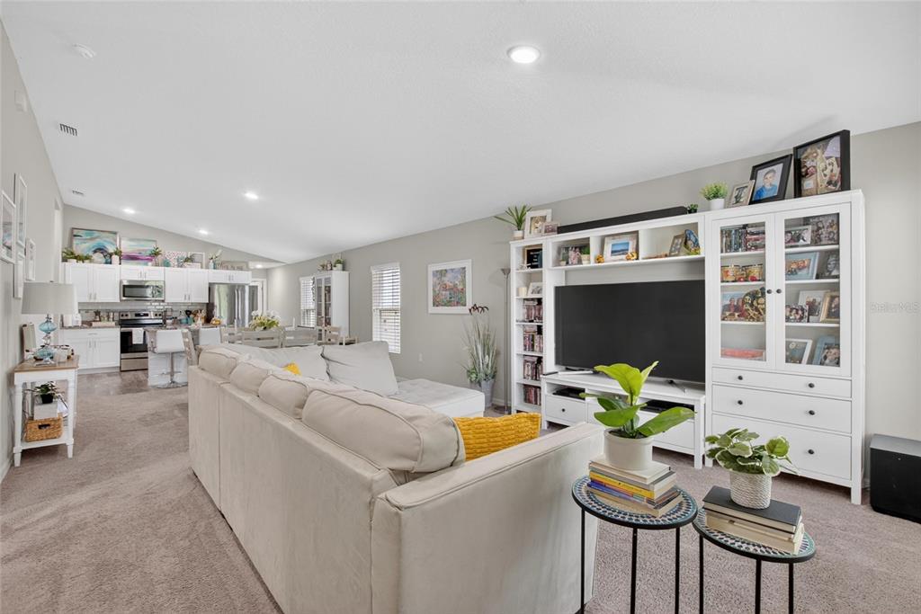 A living room with a large sectional sofa, white media center, and open-concept kitchen — 13043 PENNYBROOK DRIVE, RIVERVIEW, FL