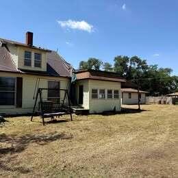 A yellow house with a porch swing and a flat-roofed addition in a grassy yard — 202 S Jefferson Avenue, KS 67003, KS