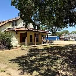 A yellow two-story house with a front porch and a metal roof under a blue sky — 202 S Jefferson Avenue, KS 67003, KS