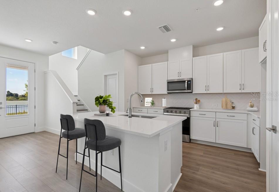 A modern kitchen features white cabinetry, a quartz island with two stools, and wood flooring — 7251 TIDELAND LANE, SARASOTA, FL
