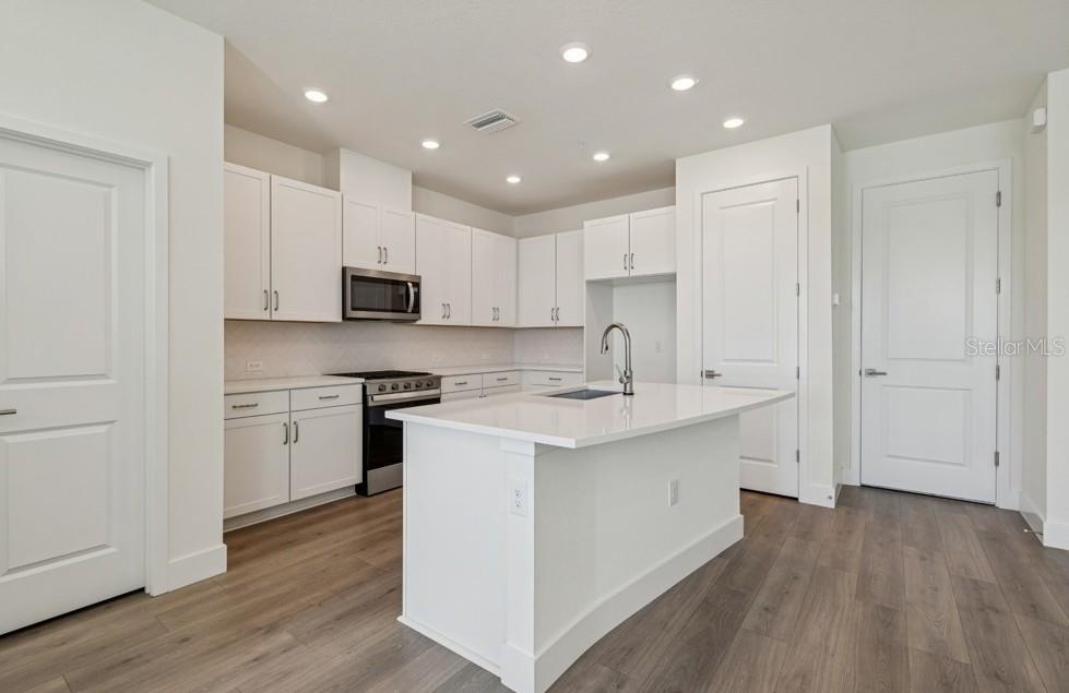 A modern kitchen features white cabinetry, a central island with a sink, and wood flooring — 7251 TIDELAND LANE, SARASOTA, FL