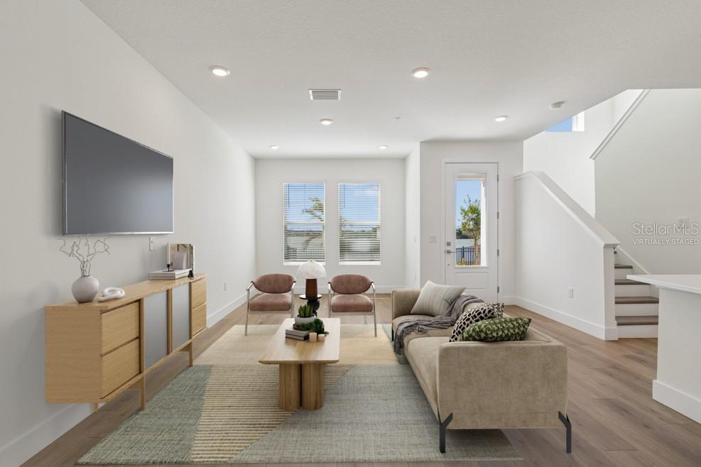 This virtually staged living room features light wood flooring, a television, and a staircase — 7251 TIDELAND LANE, SARASOTA, FL