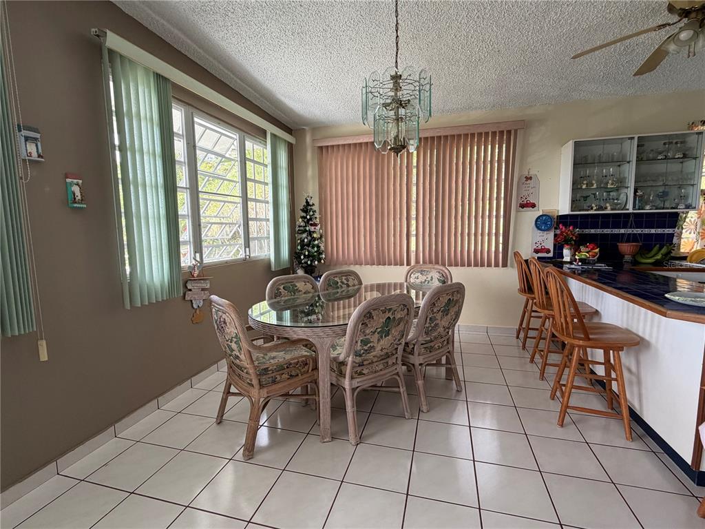 A dining area features a glass-topped table, wicker chairs, tiled floors, and a breakfast bar — Sector Flor Sanchez BO. BUENA VISTA, BAYAMON, PR