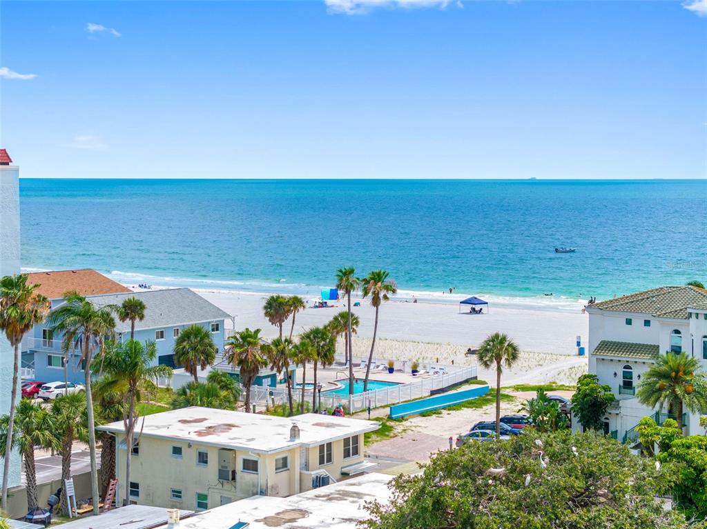 An elevated view of a beach with palm trees, a swimming pool, and nearby buildings — 18400 GULF BOULEVARD UNIT 1301, INDIAN SHORES, FL