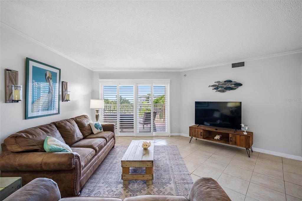 A living room features a brown leather sofa, wood coffee table, television, and sliding doors — 18400 GULF BOULEVARD UNIT 1301, INDIAN SHORES, FL