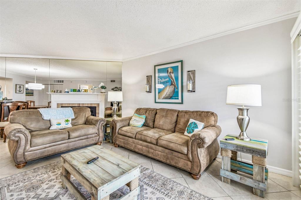 A living room features two brown sofas, a rustic coffee table, and a large wall mirror — 18400 GULF BOULEVARD UNIT 1301, INDIAN SHORES, FL