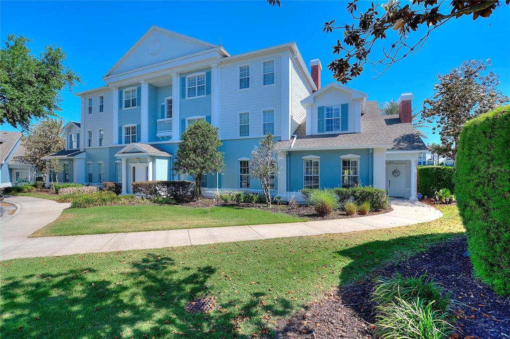 A large, multi-story blue and white house features a columned portico and manicured landscaping — 1593 HERITAGE CROSSING COURT UNIT G, REUNION, FL