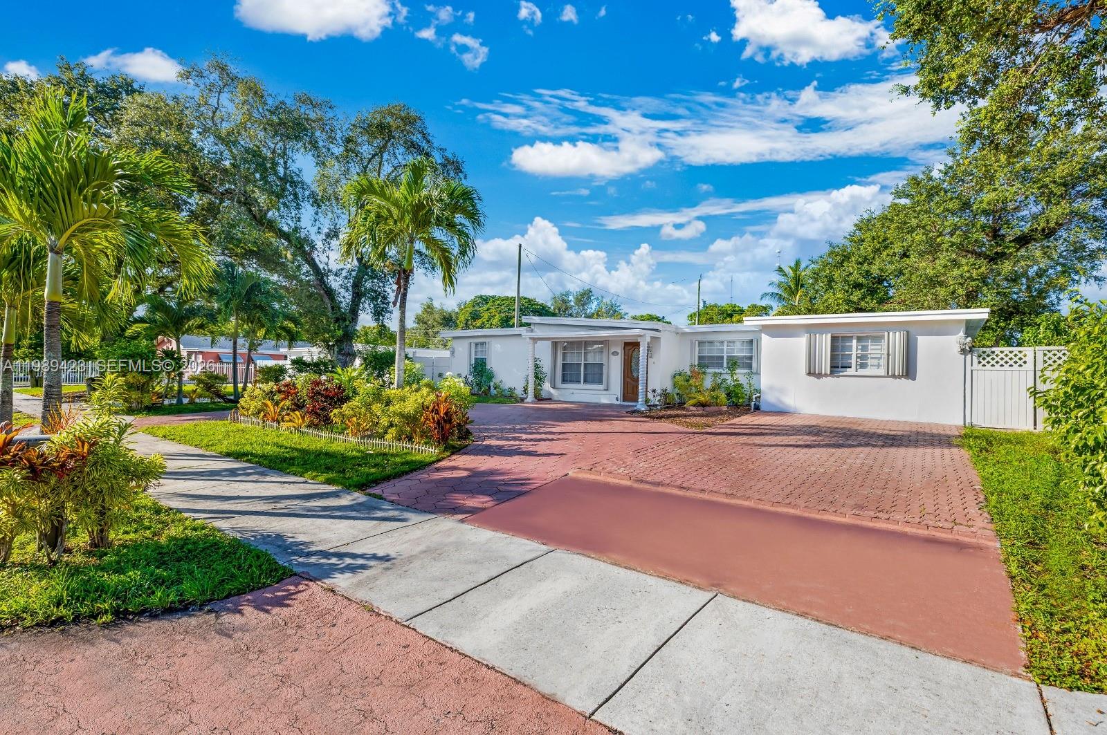A single-story white house with a red brick driveway and palm trees under a blue sky — 38 Miami Gardens Rd, West Park FL 33023, WEST PARK, FL