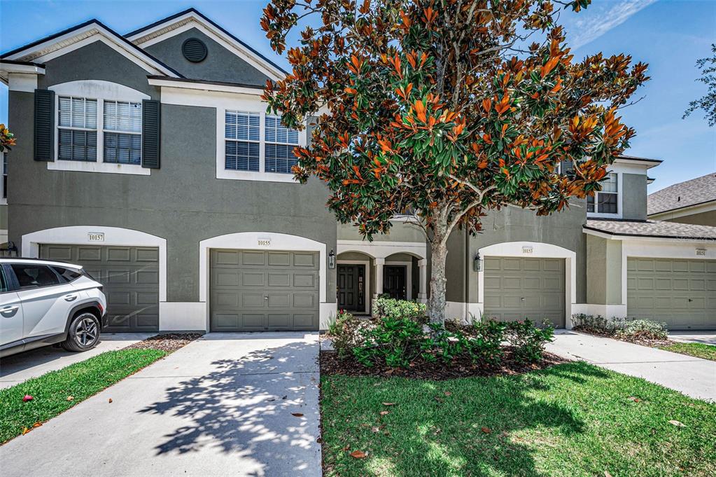 A two-story townhouse exterior features a gray facade, multiple garage doors, and a large tree — 10155 HAVERHILL RIDGE DRIVE, RIVERVIEW, FL