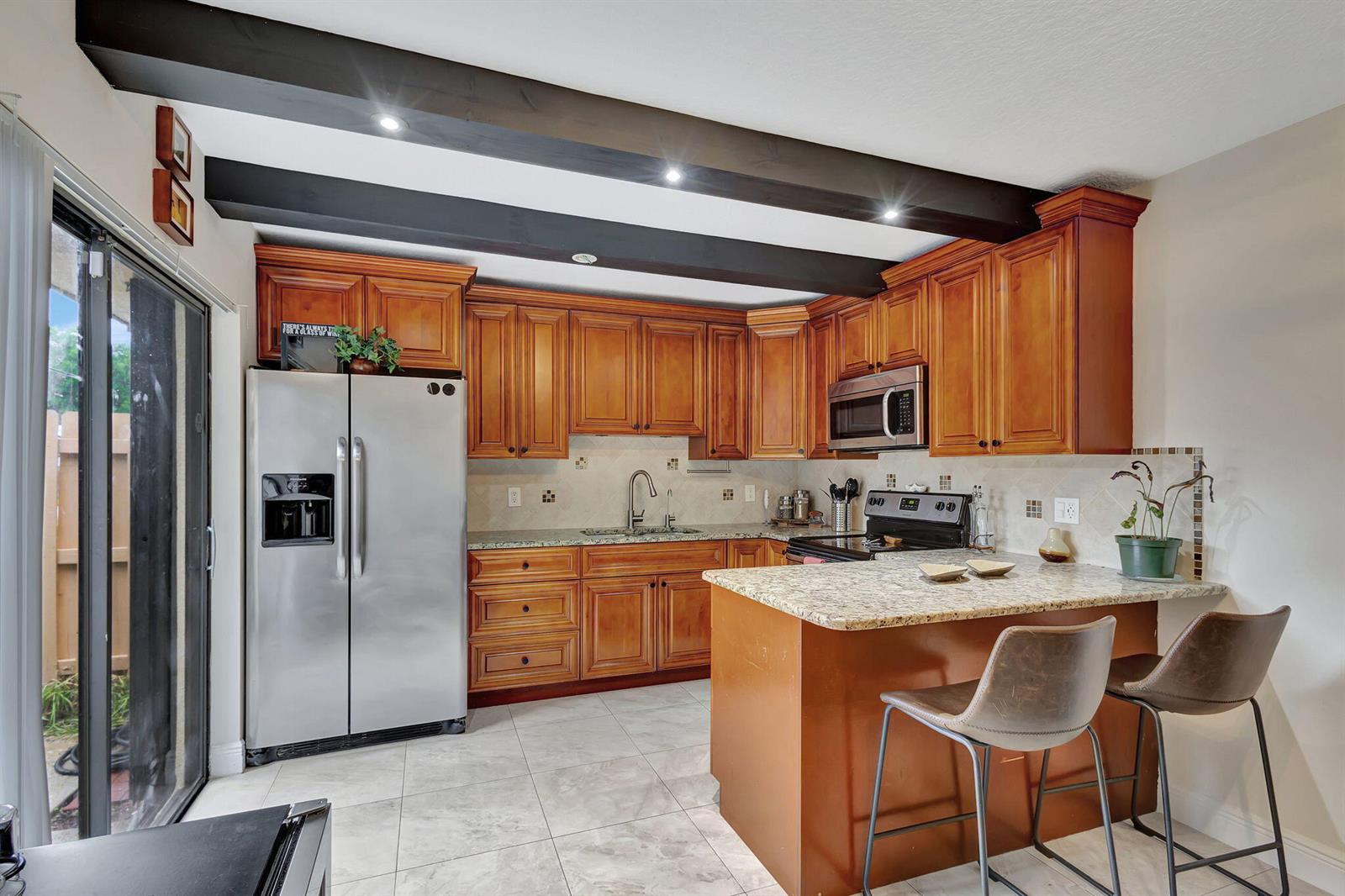 A kitchen with wood cabinets, granite countertops, stainless steel appliances, and exposed ceiling beams — 99 Lake Arbor Drive, Palm Springs FL 33461, PALM SPRINGS, FL