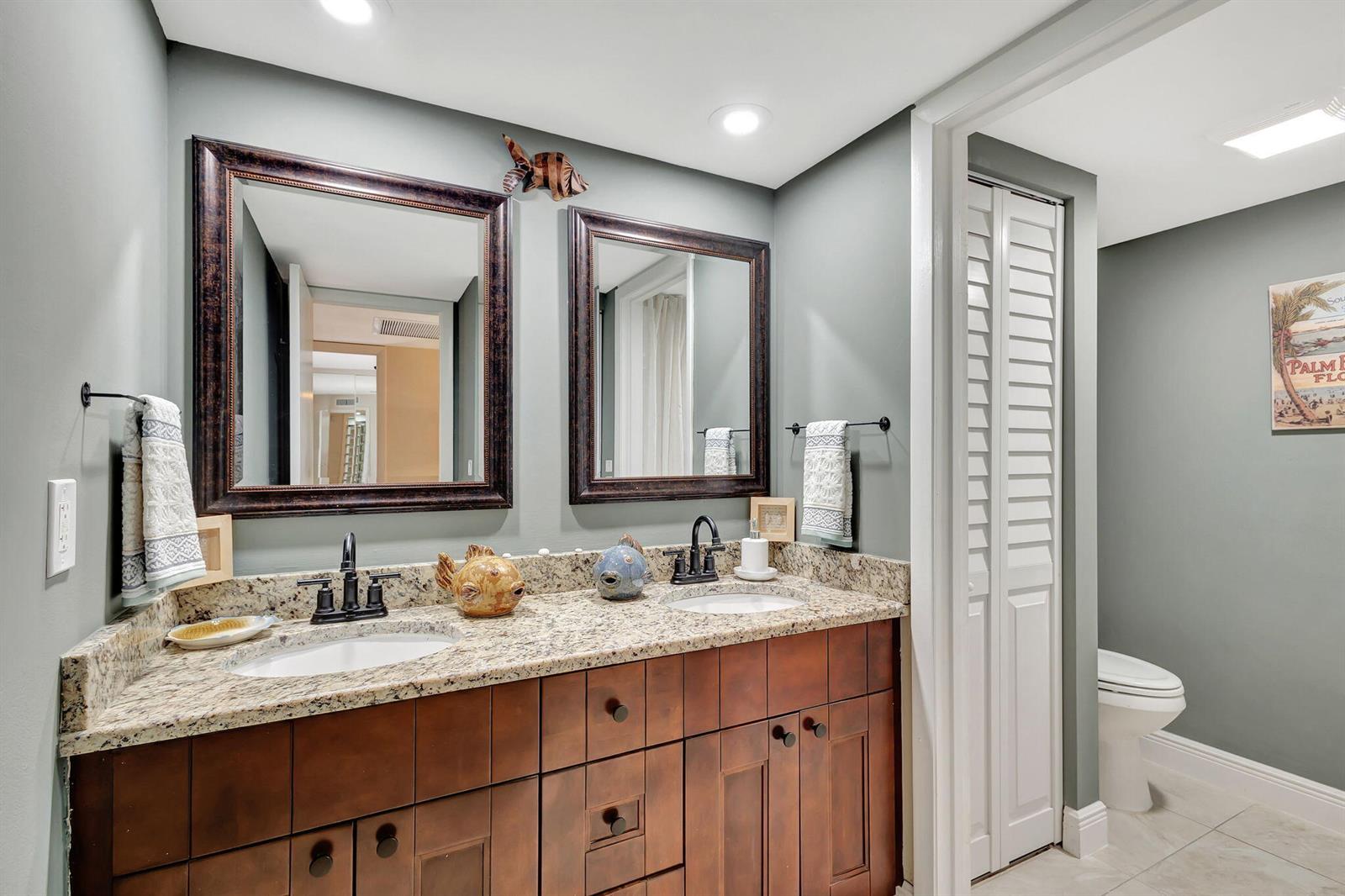 A bathroom features a double vanity with granite countertops, dark wood cabinets, and two mirrors — 99 Lake Arbor Drive, Palm Springs FL 33461, PALM SPRINGS, FL