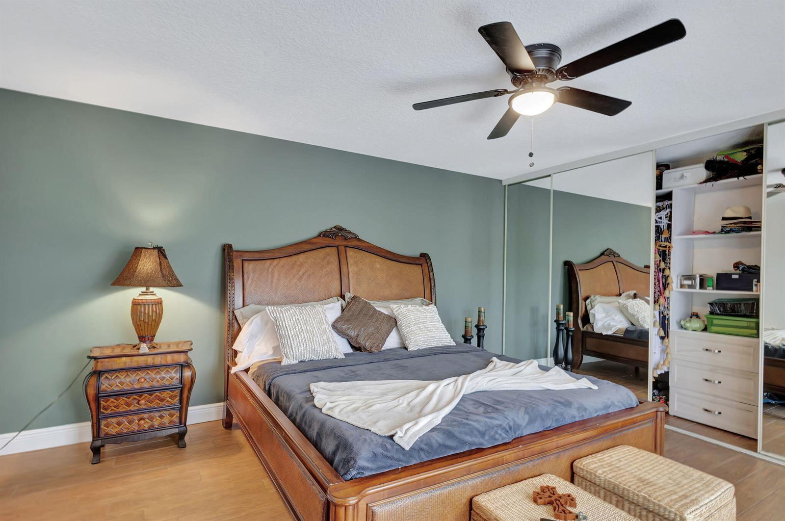 A bedroom features a wooden bed, green walls, a ceiling fan, and mirrored closet doors — 99 Lake Arbor Drive, Palm Springs FL 33461, PALM SPRINGS, FL