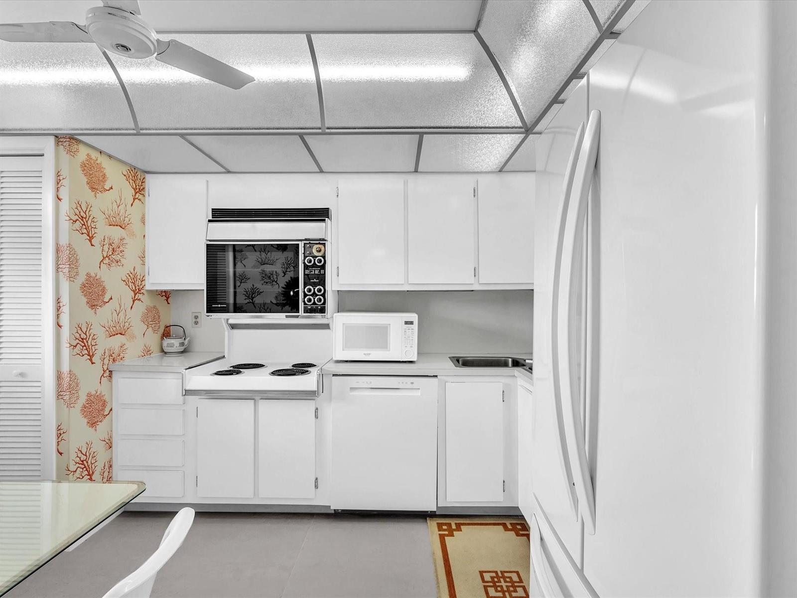 A white kitchen features a drop ceiling, coral-patterned wallpaper, and white appliances — 1537 E Hillsboro Boulevard # 438, Deerfield Beach FL 33441, DEERFIELD BEACH, FL