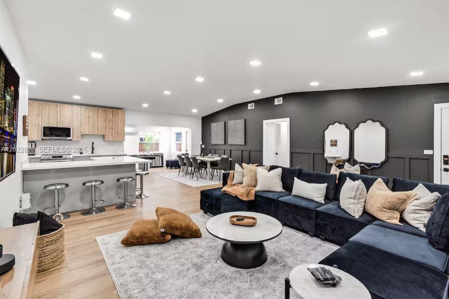 An open-concept living room and kitchen feature a dark blue sectional and wood cabinetry — 17621 NE 7th Ave, Miami FL 33162, MIAMI, FL